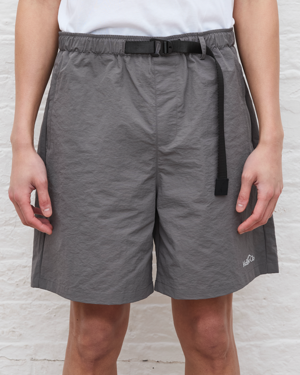 Person wearing gray shorts with a black belt on a light wooden floor.