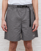 Person wearing gray shorts with a black belt on a light wooden floor.